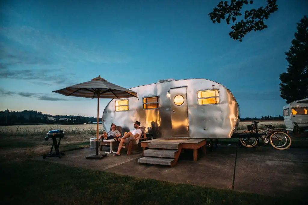 people lounging outside their brand name RV at sunset