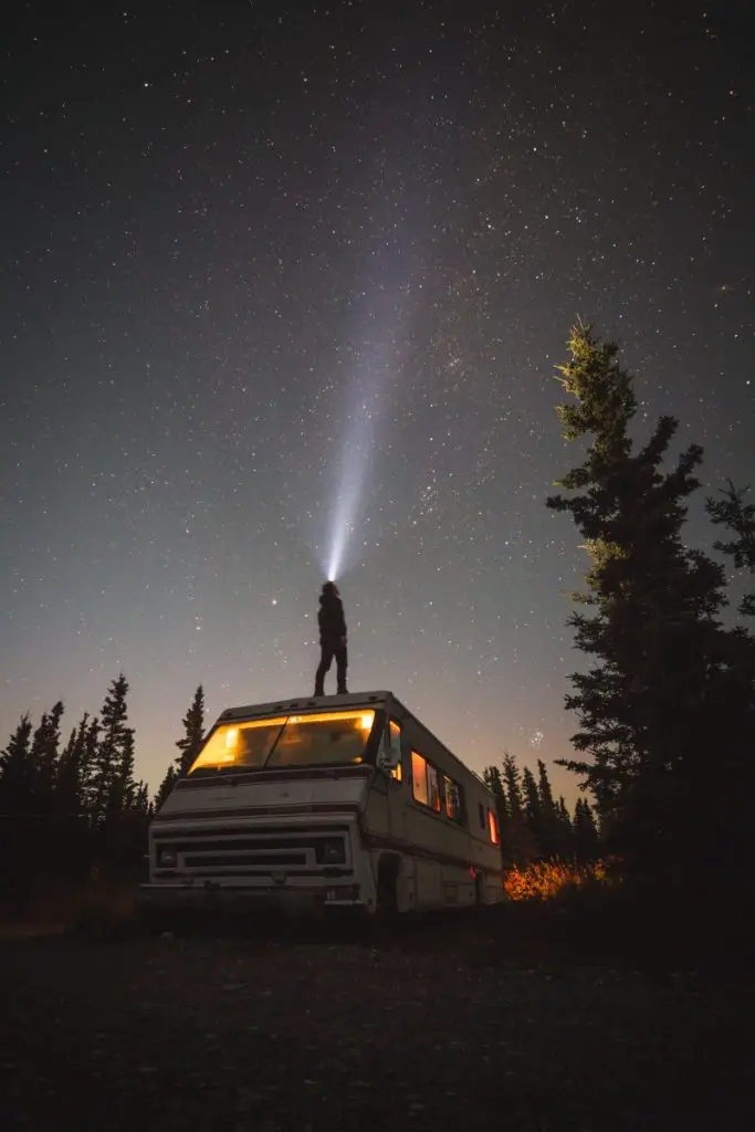 man stands on an RV shining his flashlight into the sky