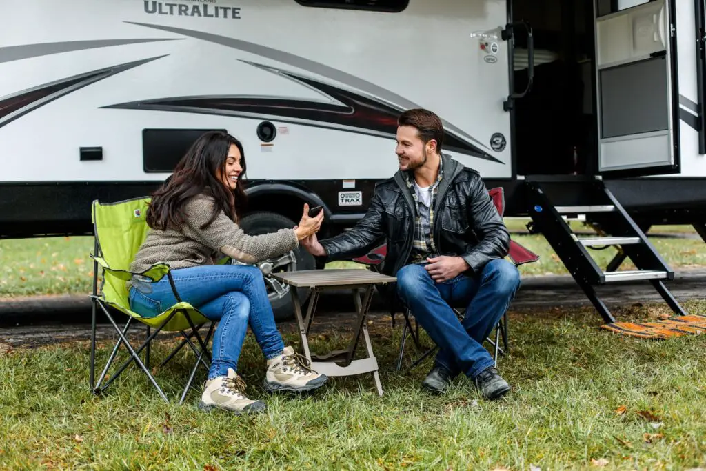 smiling man and woman sitting on chairs next to an RV