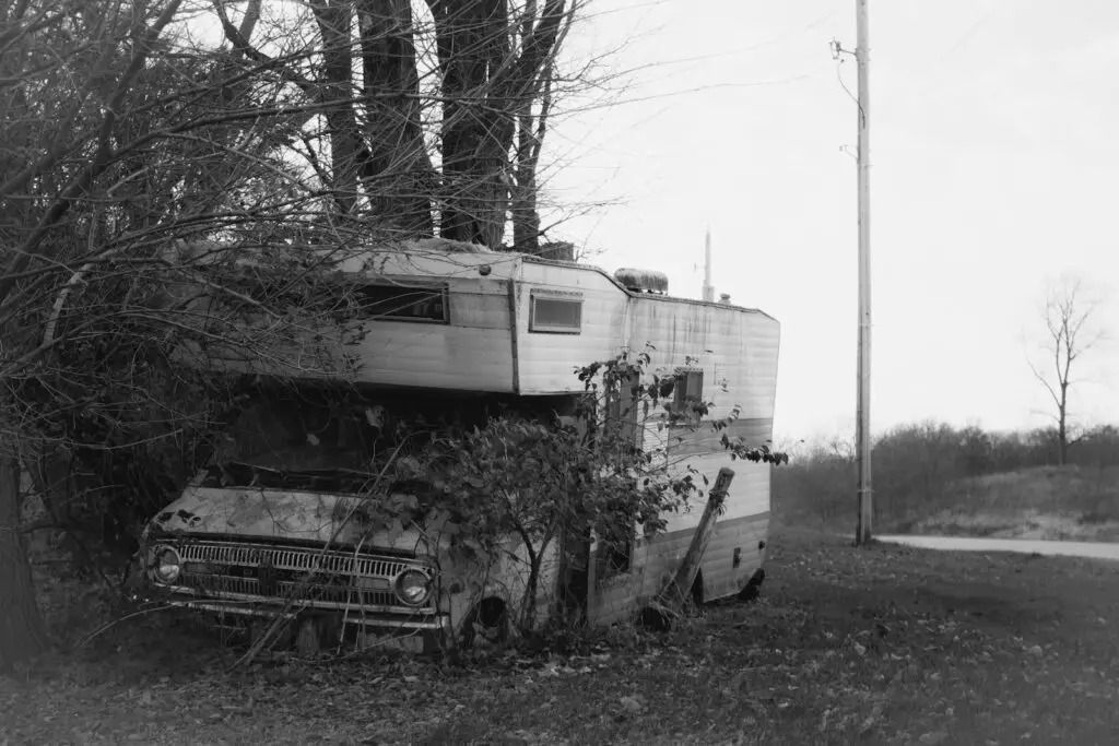 grayscale photo of a broken RV in some trees