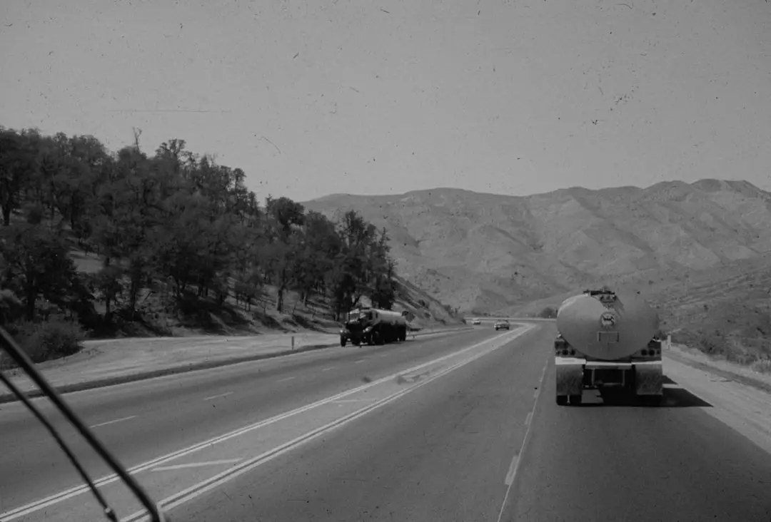 a black and white photo of a highway with a tanker truck