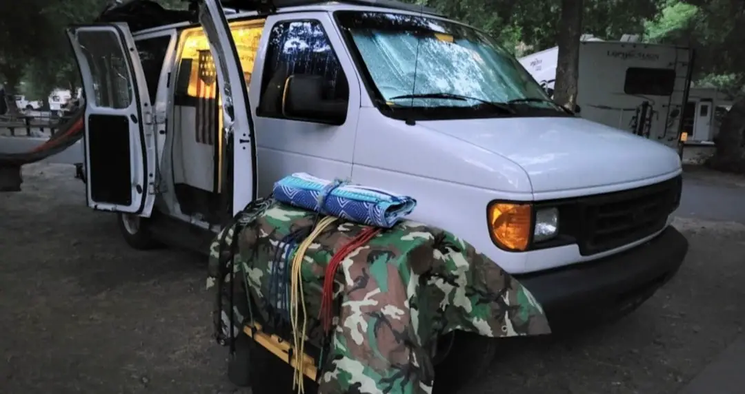 a camper van with its door open and camping gear on the ground